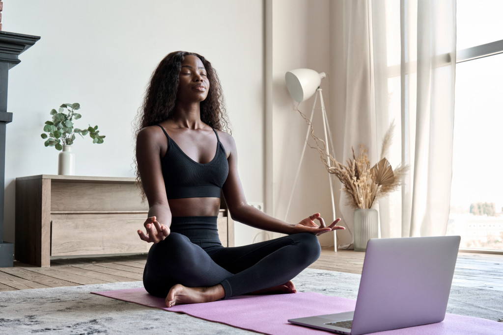 Young woman performing yoga exercises in front of her laptop.